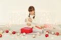 Indoor shot of child sitting on bed on oft blanket with a gift in her hands, opening box with Christmas present, posing in bedroom Royalty Free Stock Photo