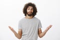 Indoor shot of clueless confused hispanic boyfriend with afro hairstyle and masculine beard, raising palms cluelessly