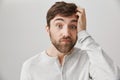 Indoor shot of clueless and puzzled attractive guy with messy beard, scratching head and looking with lifted eyebrows at