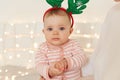 Indoor shot of cute adorable infant baby wearing striped sleeper and deer hoops, looking at camera with charming facial expression