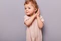 Indoor shot of cute curios little toddler caucasian girl posing isolated over gray background, baby with blond curly hair keeps Royalty Free Stock Photo