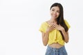 Indoor shot of cute kind and tender good-looking asian girl with dark beautiful hair holding palms on chest and smiling
