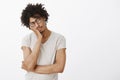 Indoor shot of cute sleepy male hispanic model with curly hair in glasses and grey t-shirt, leaning on palm, closing