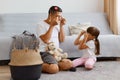 Indoor shot of dark haired male with his female child playing together at home, sitting on floor near cough in light room, making Royalty Free Stock Photo