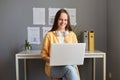 Indoor shot of delighted pleased woman with brown hair working on laptop, typing on keyboard, enjoying her online work, freelancer