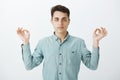 Indoor shot of determined focused attractive man in shirt, raising hands in zen gesture and staring at camera