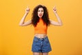 Indoor shot of displeased female client with curly stylish hairstyle red lipstick in cool cropped top pointing up