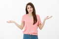 Indoor shot of displeased questioned cute brunette in pink t-shirt, spreading hands in clueless gesture, shrugging