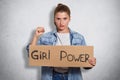 Indoor shot of energetic self confident feminist standing over grey background in studio with inscription girl power,