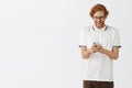 Indoor shot of entertained happy and carefree young redhead male with beard forgetting about work while messaging with Royalty Free Stock Photo
