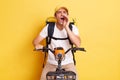 Indoor shot of excited deliveryman on bicycle wearing white T-shirt and cap isolated over yellow background, screaming