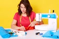 Indoor shot f concentraed woman dressmaker sewing in her studio, sitting with opened mouth, ready to sew buttons, has confident Royalty Free Stock Photo