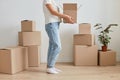 Indoor shot of faceless unknown anonymous woman wearing white t shirt and jeans, holding cardboard box with her belongings during