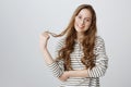 Indoor shot of friendly cute caucasian girl in transparent glasses playing with hair strand while smiling broadly over