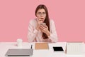 Indoor shot of frightened displeased woman holds mobile phone, has everything neatly arranged on table, recieves