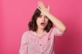 Indoor shot of frustrated forgetful young woman looking at camera with worried facial expression, holding hand on head, female