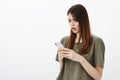 Indoor shot of frustrated unhappy cute girl in dark-green t-shirt, standing half-turned over gray background concerned