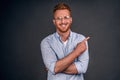 Indoor shot of good-looking confident and bossy male entrepreneur in shirt and glasses with red hair, pointing at upper right