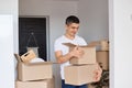 Indoor shot of handsome delighted man wearing white t shirt standing with cardboard box and looking inside, guy unpacking parcels Royalty Free Stock Photo