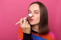 Indoor shot of happy attractive beautiful woman doing daily makeup, applying cosmetic on her hose, looking at camera with happy Royalty Free Stock Photo