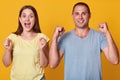 Indoor shot of happy couple marrieds clenches fists, have excited facial expressions, celebrate success, dressed in casual t Royalty Free Stock Photo