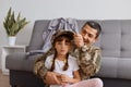 Indoor shot of happy family enjoying meeting, young adult soldier man wearing camouflage uniform returning home after army,