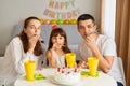 Indoor shot of happy family sitting at table celebrating birthday together, sitting at table with birthday cake and drink, blowing Royalty Free Stock Photo