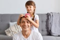 Indoor shot of happy family spending great time together, posing in living room while sitting near couch, little cute hairdresser