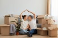 Indoor shot of happy lovely romantic couple sitting on floor surrounded with cardboard boxes during relocation to a new apartment Royalty Free Stock Photo
