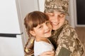 Indoor shot of happy military woman wearing camouflage uniform returning home after army, meeting her lovely daughter, hugging her Royalty Free Stock Photo