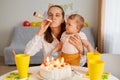 Indoor shot of happy mother and her infant daughter posing at home while sitting at table with birthday cake and candles, mommy Royalty Free Stock Photo