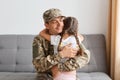 Indoor shot of happy soldier man in camouflage hugging his daughter with closed eyes, missing her kid very much, sitting on sofa Royalty Free Stock Photo