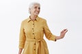 Indoor shot of happy stylish and pretty elegant senior woman in trendy yellow coat posing with ellegance over gray Royalty Free Stock Photo