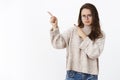 Indoor shot of intense displeased and hesitant young charming woman in glasses and sweater, frowning and pursing lips in