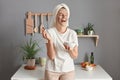 Indoor shot of laughing beautiful young woman with bath towel on her head, applying lifting hydrating moisturizing facial mask to Royalty Free Stock Photo