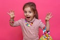 Indoor shot of little funny girl trying to frighten her friends or parents, keeping hands up, screaming like monster, wearing