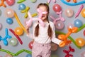 Indoor shot of little girl with braids wearing casual clothing posing isolated over gray background with balloons, holding air Royalty Free Stock Photo