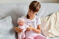 Indoor shot of little girl sitting on the sofa in the room at home playing with baby doll, like mom, dark haired preschooler Royalty Free Stock Photo