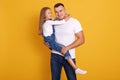 Indoor shot of loving daddy holding at little adorable daughter feeling love isolated over yellow studio background. Deep devotion
