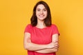 Indoor shot of magnetic beautiful young girl standing with folded arms, looking directly at camera, having sincere smile on her