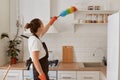 Indoor shot of maid wiping the dust with ppduster in the kitchen, housewife with bun hairstyle doing household chores, cleaning Royalty Free Stock Photo