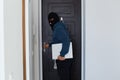 Indoor shot of male burglar wearing dark blue hoodie and black mask stands at the door of the house he robbed, trying to hide
