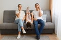 Indoor shot of man and woman wearing jeans and white t shirts sitting on sofa and talking on smart phones, their daughter lying Royalty Free Stock Photo