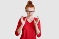 Indoor shot of outraged woman gestures angrily, has frowned expression, wears spectacles and red clothes, looks with