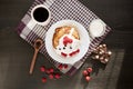 Indoor shot of pancakes with multiple berries and sour cream, cup of coffee or tea, spoon, chocholate pieces on dark surface,