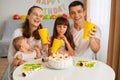 Indoor shot of parents and children celebrating birthday together, sitting at table with birthday cake and drink, looking at Royalty Free Stock Photo