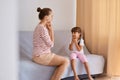 Indoor shot of pleasant looking woman speech pathologist having lesson with little girl, people sitting on comfortable sofa near