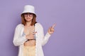 Indoor shot of pleasant surprised woman wearing panama, white shirt and swimming suit, pointing away at advertisement area, copy Royalty Free Stock Photo