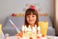 Indoor shot of pretty girl celebrating birthday party, smiling, having happy positive emotion, looking at cake with candles with Royalty Free Stock Photo