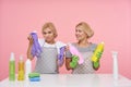 Indoor shot of pretty young blonde housewives dressed in basic t-shirts and aprons sitting over pink background with multi-colored Royalty Free Stock Photo